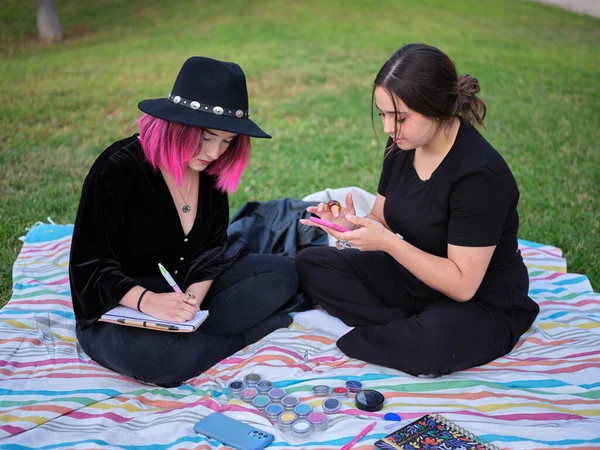 Zwei junge Mädchen sitzen auf einer Decke im Park und entwerfen Make-up — Stockfoto