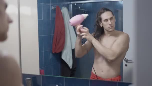 Jonge metroseksuele man met behulp van een haardroger in de voorkant van de badkamer spiegel na een douche - Time lapse — Stockvideo