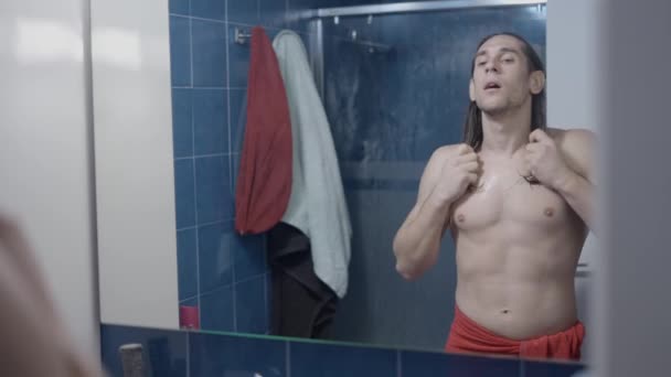 Jonge metroseksuele man drogen zijn haar in de voorkant van de badkamer spiegel na een douche met zijn handen - Midden schot — Stockvideo