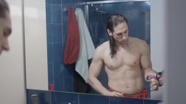 Jonge metroseksuele man neemt uit een lade een pin haardroger en droog zijn haar in de voorkant van een spiegel - MIddle shot — Stockvideo