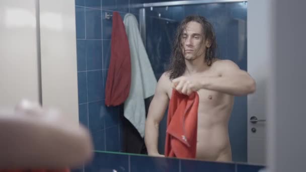 Jonge metroseksuele man drogen zijn haar in de voorkant van de badkamer spiegel na een douche met een rode handdoek - Midden schot — Stockvideo