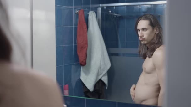 Fiatal fitt férfi nézi a hasát a fürdőszoba tükörben - középső lövés — Stock videók