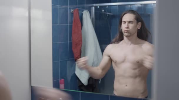 Jonge naakte man slaat zichzelf als een aap in de voorkant van de badkamer spiegel - Midden schot — Stockvideo