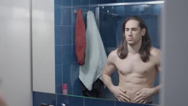 Jong naakt op zoek naar zijn buikspieren in de voorkant van de badkamer spiegel - Midden schot — Stockvideo