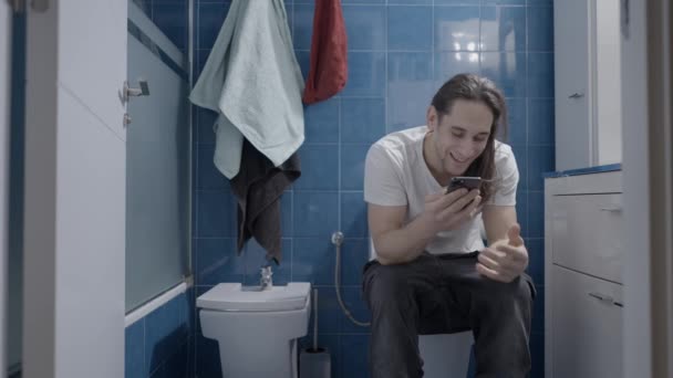 Homem caucasiano jovem enviando uma mensagem de áudio com seu telefone no banheiro - tiro frontal — Vídeo de Stock