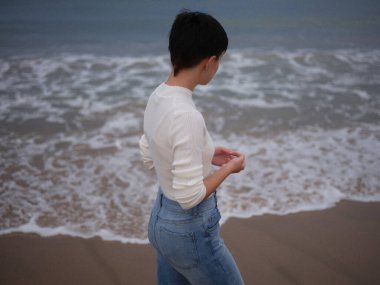 Kadın denizin önünde durmuş dalgaların hareket edişini izliyor.