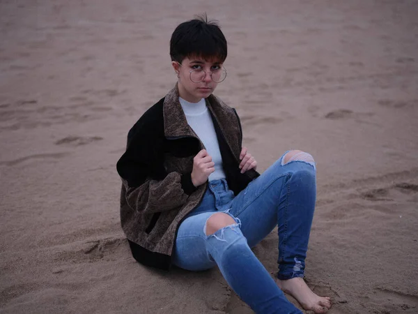 Transgender person sitting on the sand with a jacket and glasses — Fotografia de Stock