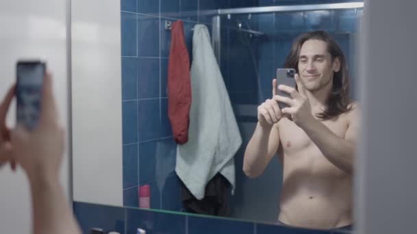 Jonge naakte man doet een selfie in zijn badkamer spiegel - slow motion shot — Stockvideo