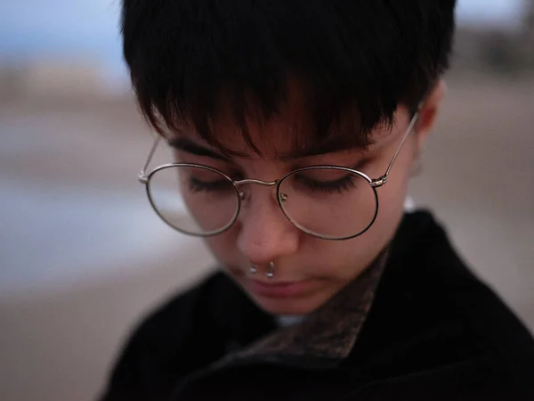 Close-up view of the face of a young transgender girl with glasses and septum looking down — Fotografia de Stock