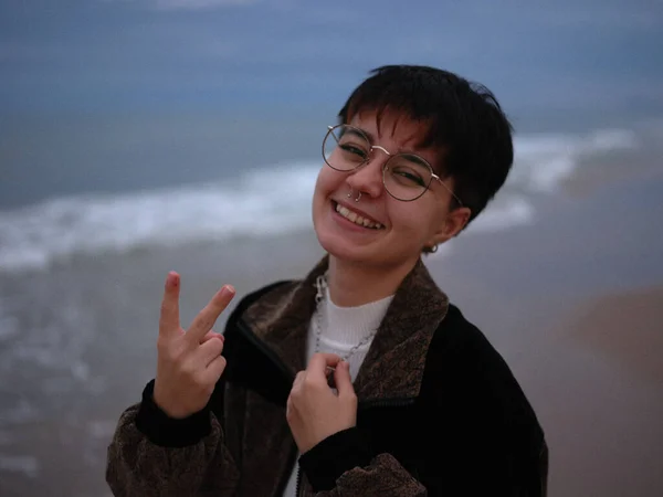 Chica transexual sonriente de pie en la playa haciendo señal de victoria con su mano — Foto de Stock