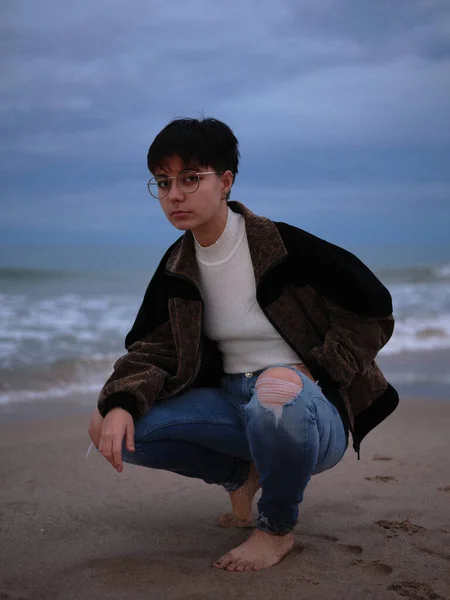 Woman squatting barefoot posing on the seashore wearing long trousers and jacket — 图库照片