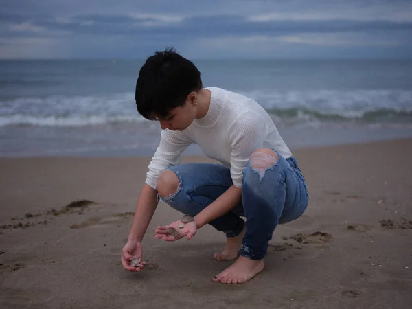 Небінарна жінка збирає раковини з піску на пляжі — стокове фото