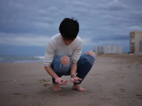 Молода дівчина присідає на пляжі шукає мушлі в піску — стокове фото