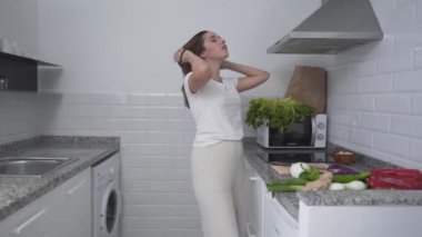 Young Female Is Tying Her Hair Before Cooking At Home Kitchen. Medium Shot