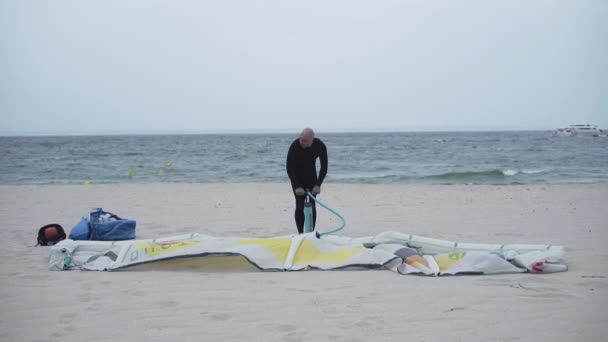 Man pumping an inflatable kite on the sand beach. — Stockvideo