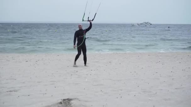 Kitesurfer masculino en traje de neopreno en la costa de Mallorca en España con barra de control de cometas en la arena. dolly-in — Vídeo de stock