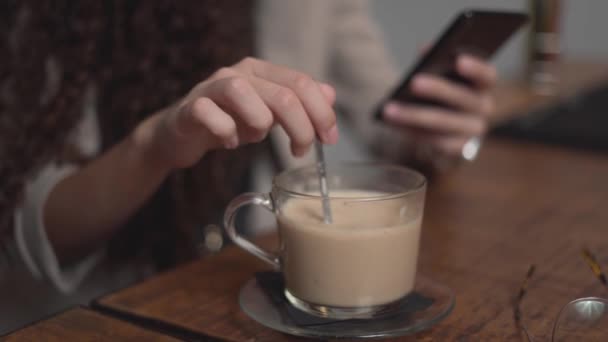 Curly-Haired mulher mexa e bebe café enquanto estiver usando celular. Fechar — Vídeo de Stock