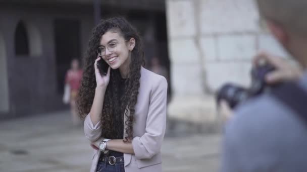 Fotógrafo masculino tomando fotos de una joven marroquí sonriendo mientras llama al teléfono móvil. foco de rack — Vídeo de stock
