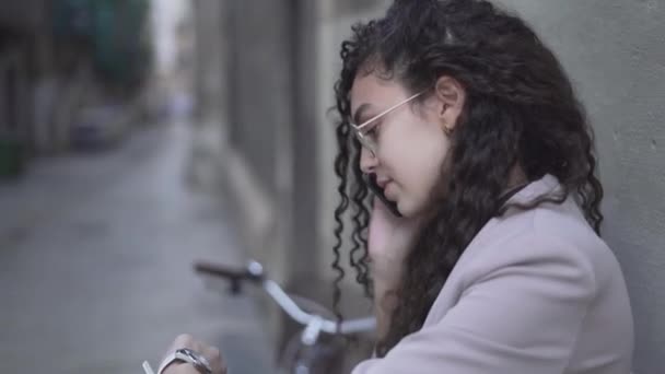 Long Curly-Haired Moroccan Girl Looking On Her Wristwatch While Talking On A Smartphone. Zoom out — Stock video