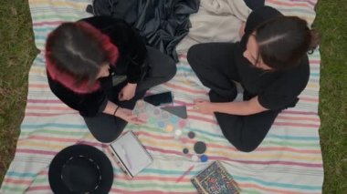 birds eye over two girls on black clothes sitting on a colored mat, chatting about cosmetics makeup