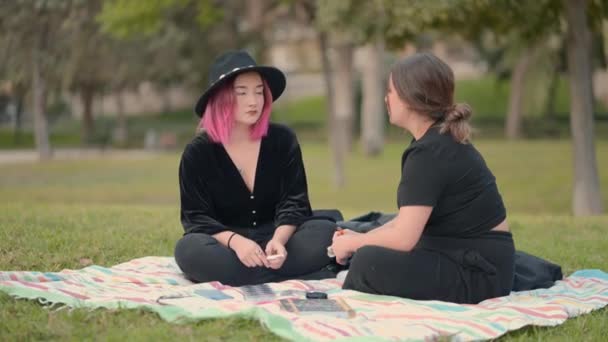 Кавказские девушки разговаривают, сидя на траве в парке. широкий вид — стоковое видео