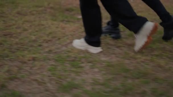 Pares de piernas y zapatillas de deporte caminando sincrónicamente sobre la hierba. vista de ángulo bajo — Vídeos de Stock
