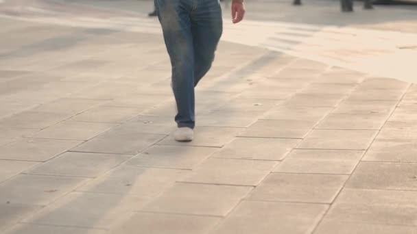Iemand benen gekleed in jeans en sneakers lopen op de stoep, laag zicht, slow motion — Stockvideo