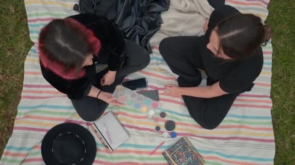 Birds eye over two girls on black clothes sitting on a colored mat, chatting about cosmetics makeup — 图库视频影像