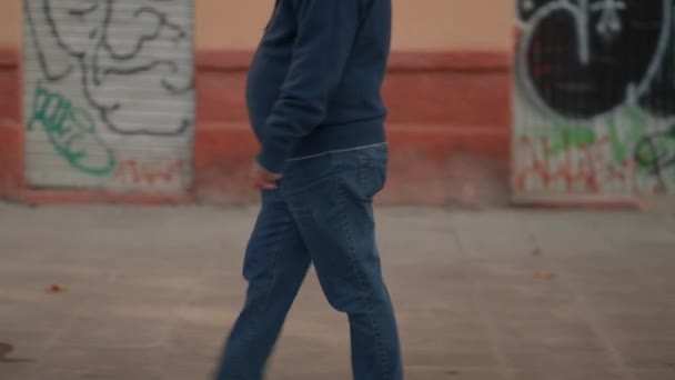 Man dressed in jeans and sweater walking on sidewalk, lower body. slowmotion, tracking shot — Stok video