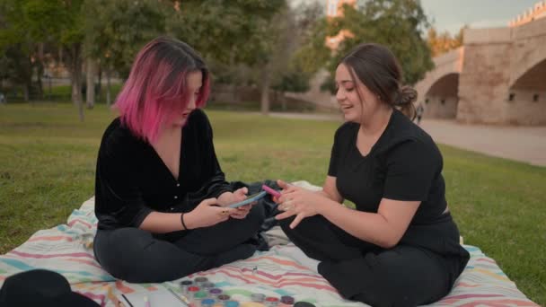 Young women sitting on ground at park area, focusing on smartphone screen. slowmotion — Vídeo de stock
