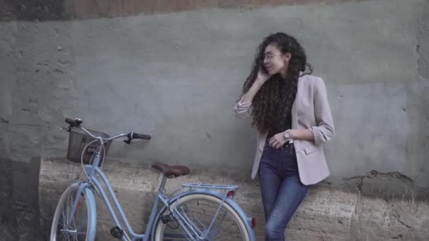 Marockanska flicka lutar sig på betong vägg gör ett telefonsamtal med cykel. - medelstora skott — Stockvideo