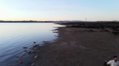 Torrevieja Pembe Gölü boyunca koşan bir adam elinde bir gitar tutuyor - günbatımında anten.