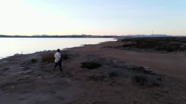 Gün batımında Torrevieja Pembe Gölü boyunca koşan gitarlı adam, Alicante - hava görüntüsü, yavaş motin