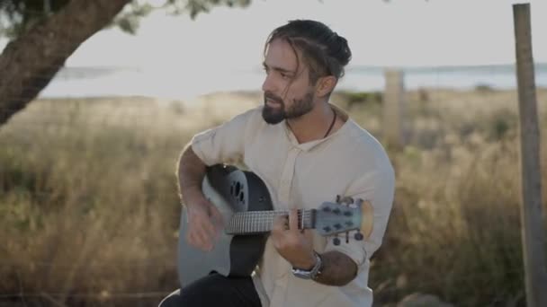 Bel homme guitariste strumming sur classique guitare acoustique et chant chanson regardant objectif de la caméra dans la campagne Espagne au coucher du soleil — Video