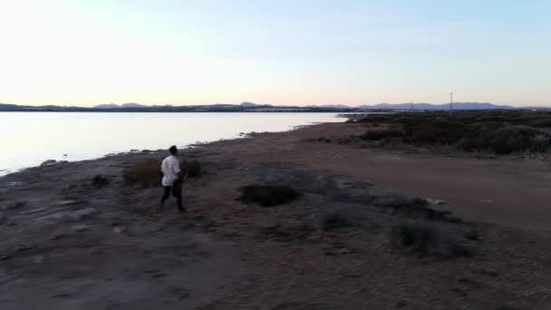 Mannen med gitarren kör längs Torrevieja Rosa sjön vid solnedgången, Alicante - antenn skott, slow-motin — Stockvideo