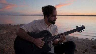Sahilde gitar çalan genç bir adamın silueti. 