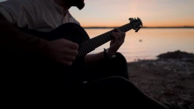 Gölün kıyısında gitar çalan bir adamın silüetli elleri - yavaş çekim