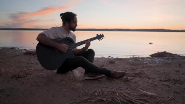 Silueta de un joven en la playa con una guitarra tocando acordes por Torrevieja Pink lake en Alicante, España al atardecer — Vídeo de stock