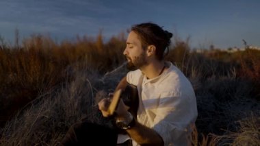 Erkek müzisyen sonbaharda günbatımında gitar çalıp şarkı söylüyor.