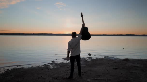 Silhuett man håller en gitarr upp i luften medan du tittar på fantastisk gyllene solnedgång över Torrevieja Rosa sjön i Alicante, Spanien — Stockvideo