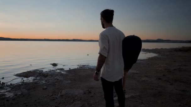 Mannen med gitarr njuter av solnedgången utsikt stående vid Torrevieja Rosa sjön i Alicante, Spanien — Stockvideo