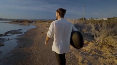 Gün batımında kumlu nehir kıyısında yürüyen gitarlı bir erkek, Alicante, İspanya 