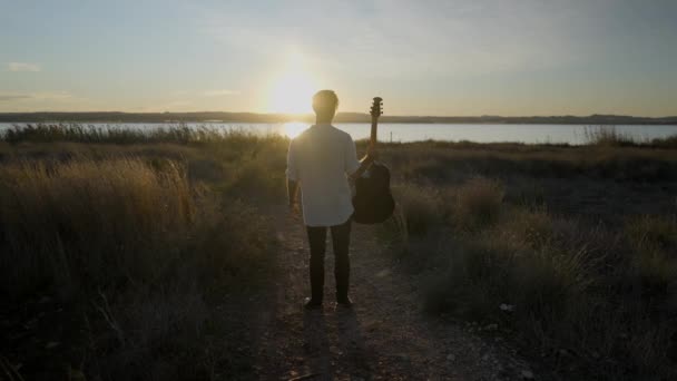 Homme au silhouette avec guitare sautant et frappant des jambes contre un soleil couchant - Vue arrière au ralenti — Video