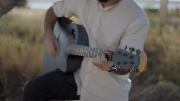 Homme hipster barbu hispanique jouant de la guitare au bord de la route à la campagne - retrait, ralenti — Video