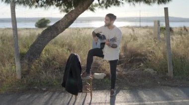 İspanyol maço adam akustik gitar tıngırdatıyor yol kenarında duruyor ve şarkı söylüyor kırsal kesimde günbatımında kameraya bakıyor yavaş çekimde İspanya 'da