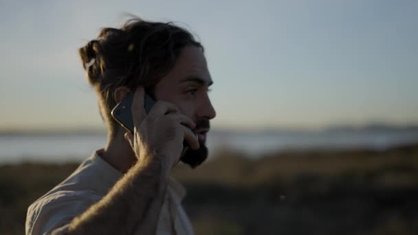 Gros plan du visage de l'homme barbu parlant au téléphone à l'extérieur au coucher du soleil au ralenti — Video