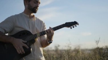 Sonbaharda gün batımında açık gökyüzünün altında gitar çalan sakallı İspanyol gitarist portresi. 