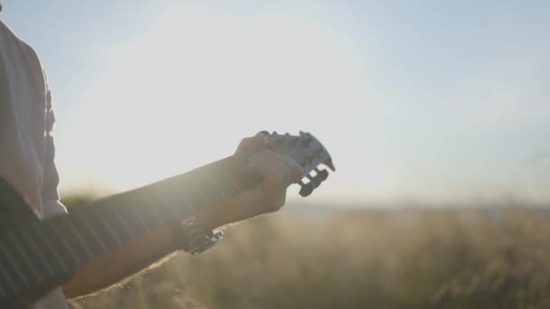 Man gitarrist spelar gitarr i gräsplan vid solnedgången - bakgrundsbelyst skott — Stockvideo