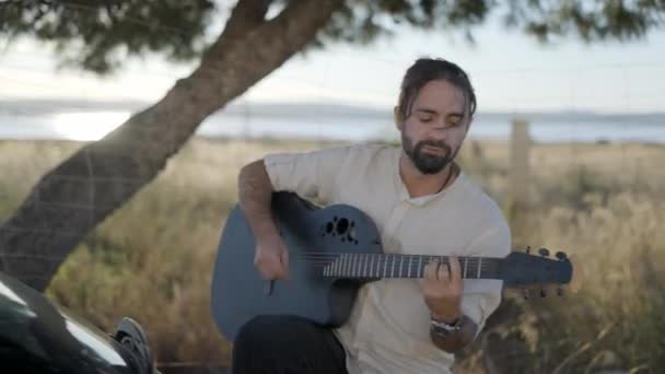 Szakállas férfi gitározik a szabadban közel az autó és énekel ritmikus agilis dal Road side — Stock videók