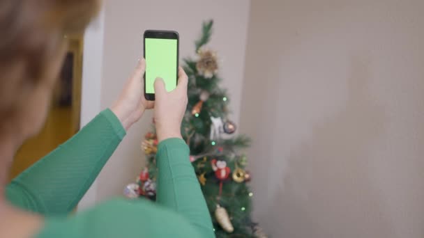 Oude Spaanse vrouw neemt foto 's van kerstboom met mobiele telefoon met groen scherm. - Sluiten. — Stockvideo